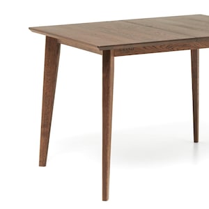 May include: A rectangular wooden table with a natural brown finish. The table has four tapered legs and a simple, modern design. The word "GRAND" is visible on the side of the table.