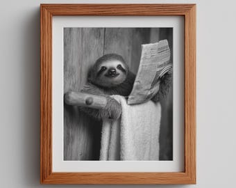 May include: Black and white framed print of a sloth reading a newspaper while sitting on a towel rack. The sloth is smiling and appears to be enjoying the newspaper. The frame is made of wood.