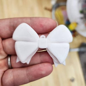 May include: A white plastic bow ornament with a loop at the top for hanging.