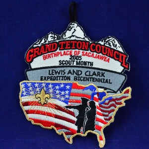 Puede incluir: Parche bordado con el logotipo del Grand Teton Council, el texto "Birthplace of Sacajawea" y el año 2005. El parche incluye un contorno de los Estados Unidos con un diseño de bandera estadounidense y siluetas de Lewis y Clark.