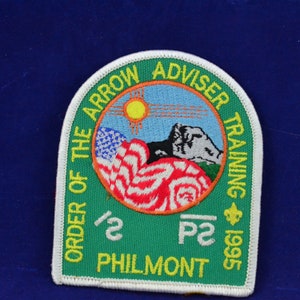 Puede incluir: Parche bordado verde y blanco con el texto "ORDER OF THE ARROW ADVISER TRAINING 1995". El parche presenta una bandera estadounidense, un sol, montañas y el texto "PHILMONT".