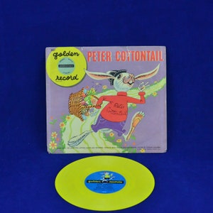 以下が含まれることがあります： ピーター・コットンテールをフィーチャーした、ヴィンテージのゴールデンレコードのアルバムカバーとレコード。アルバムカバーは紫で、ウサギが卵のバスケットを持っているイラストが描かれています。レコードは黄色で、青と金のラベルが付いています。