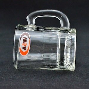 May include: Clear glass mug with a rectangular shape and a curved handle. The mug features the A&W logo in orange, brown, and white on the front. The mug is designed with a grid pattern on the sides.