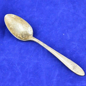 Puede incluir: Una cucharita de plata con un diseño floral en el mango. La cuchara tiene un cuenco redondeado y un mango largo y delgado.