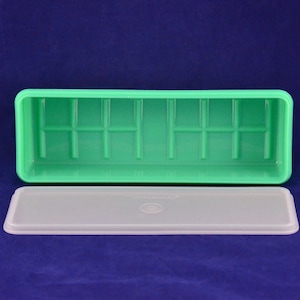 May include: A rectangular mint green plastic storage container with a grid-patterned base and a separate, translucent white rectangular lid. The lid features a centred circular embossed detail and the brand name Tupperware printed on it.