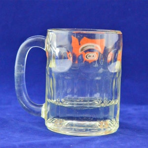 May include: A clear glass mug with a handle. The mug has a ribbed design and a logo that says "WA" in a circle. The logo is orange and white.