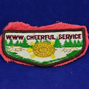 Könnte beinhalten: Ein weißer gestickter Aufnäher mit grünem und braunem Rand. Der Aufnäher zeigt eine Schildkröte mit gelber Schale und grünen Beinen, umgeben von grünen Bäumen und einer braunen Brücke. Der Text "WWW CHEERFUL SERVICE" ist in Maroon gestickt.