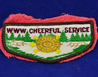 May include: A white embroidered patch with a green and brown border. The patch features a turtle with a yellow shell and green legs, surrounded by green trees and a brown bridge. The text "WWW CHEERFUL SERVICE" is embroidered in maroon.