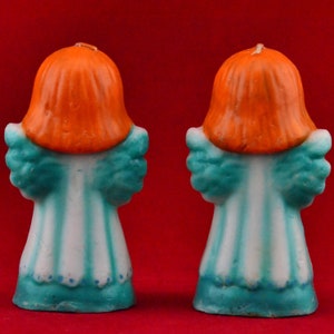 May include: Two teal blue and white angel candle holders with orange hair. The candles are made of wax and have a vintage look.