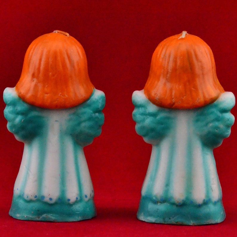 May include: Two teal blue and white angel candle holders with orange hair. The candles are made of wax and have a vintage look.