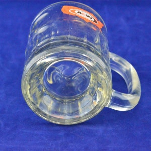 May include: A clear glass mug with a handle. The mug has a raised A&W logo on the side. The logo is orange and white.