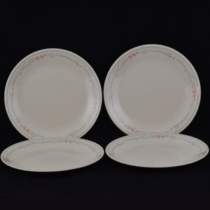 May include: A set of four white ceramic plates with a grey and coral floral border. The set includes two large round plates and two smaller oval plates, set against a black background.