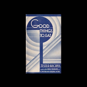 May include: A vintage cookbook cover with a blue and white art deco design. The title "GOOD THINGS TO EAT" is displayed in large, stylized white letters. Below, the text "TESTED RECIPES" is visible, along with the baking soda brands.