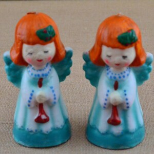 May include: Two small, blue and white angel candle holders with red trumpets. The angels have orange hair and green holly leaves on their heads.