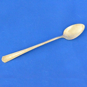 May include: A silver teaspoon with a rounded bowl and a long, slender handle. The spoon has a slightly worn appearance.