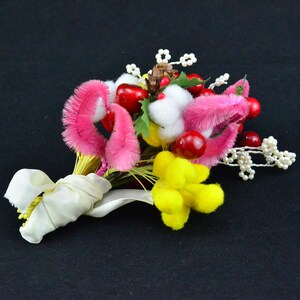 May include: A vibrant, handmade bouquet with pink, yellow, and white elements. The arrangement includes red berries, faux cotton, and a cream ribbon. The bouquet is tied with a cream-coloured ribbon.
