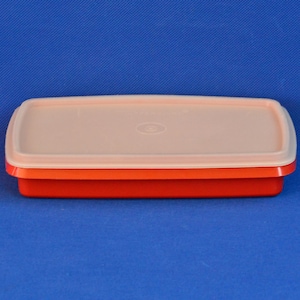 Op de afbeelding: Een rechthoekige opbergbak met een feloranje onderkant en een lichtbeige deksel. Het deksel is voorzien van een gecentreerde cirkelvormige inkeping. De bak heeft gladde, afgeronde hoeken en een plat ontwerp voor opslag of stapelen.