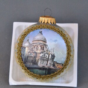 May include: A round, blue and gold Christmas ornament with a picture of a church in Venice, Italy. The ornament has a gold trim and a gold ribbon.