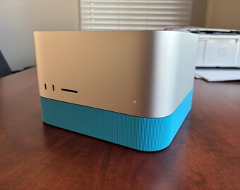 Puede incluir: Un dispositivo electrónico rectangular de color plateado con una parte superior metálica lisa y una base texturizada de color azul brillante. El panel frontal presenta dos ranuras verticales, una horizontal y una pequeña luz blanca.