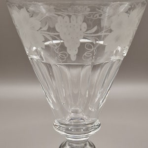 May include: A clear glass goblet with a fluted stem and a square base. The goblet is etched with a design of grapes and vines.