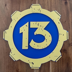 May include: A yellow gear-shaped sign with a blue circle in the center. The number 13 is printed in yellow inside the circle.
