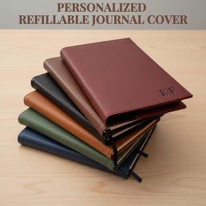 May include: A stack of personalized refillable journal covers in various colors, including burgundy, brown, black, tan, green, and navy blue. The top journal is burgundy with initials "EF" embossed. The text "PERSONALIZED REFILLABLE JOURNAL COVER" is at the top.