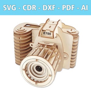 Op de afbeelding: Een houten model van een camera met de tekst "E700" aan de bovenkant. De camera is gemaakt van lichtgekleurd hout en heeft een gedetailleerd ontwerp. De bovenkant van de afbeelding bevat de tekst "SVG - CDR - DXF - PDF - AI".