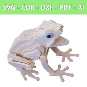 May include: A wooden frog puzzle with a light beige finish. The frog has blue eyes and is assembled from multiple layered pieces. The image includes the text "SVG - CDR - DXF - PDF - AI" in a green banner at the top.