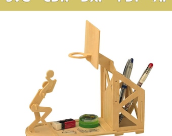 Op de afbeelding: Een lichtgekleurde houten bureau-organizer in de vorm van een basketbalveld met een ring, een speelfiguur en een pennenhouder. De basis bevat een kleine gum en een groene container. Tekst bovenaan luidt SVG - CDR - DXF - PDF - AI.