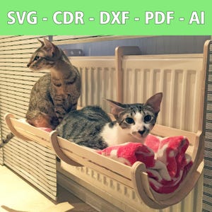 Könnte beinhalten: Zwei Katzen entspannen sich auf einem Holzkatzenbett, das an einem Heizkörper befestigt ist. Das Bett ist aus Holz und hat ein rosa Handtuch drin. Die Katzen schauen beide in die Kamera.