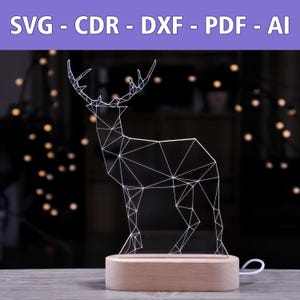 Könnte beinhalten: Ein weißes geometrisches Hirsch-Nachtlicht auf einem Holzsockel. Der Hirsch ist aus einem klaren Material gefertigt und hat einen Drahtrahmen.