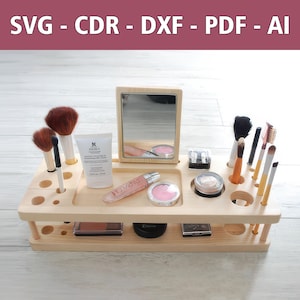 Puede incluir: Un organizador de maquillaje de madera con dos estantes. El estante superior tiene un espejo, un pequeño recipiente de rubor y una botella transparente de líquido. El estante inferior tiene dos pequeños recipientes de sombra de ojos y un pequeño recipiente de brillo de labios. También hay varios pinceles de maquillaje en el organizador.