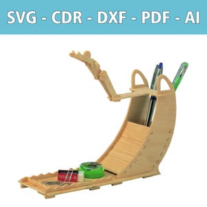 May include: A light-colored wooden desk organizer featuring a ramp-like structure with a small articulated figure at the top. The unit includes a pen holder, a flat base for small items, and text at the top reading SVG - CDR - DXF - PDF - AI.