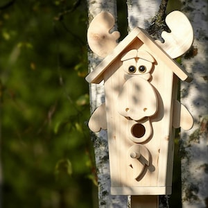 May include: A wooden birdhouse shaped like a moose with large, exaggerated eyes and a wide, open mouth. The birdhouse is painted in a natural wood color and has a small opening for birds to enter.