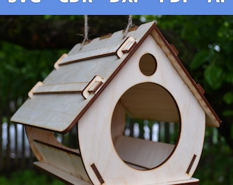 Könnte beinhalten: Ein hölzerner Vogelhäuschen in Form eines Hauses mit einem schrägen Dach und einer runden Öffnung, durch die Vögel an das Futter gelangen können. Der Futterspender ist aus hellem Holz gefertigt und hat einen kleinen Sitzplatz am Boden.