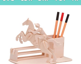 Op de afbeelding: Een bureau-organizer van lichtgekleurd hout met een lasergesneden ontwerp van een paard en ruiter die over een hindernis springen. De structuur bevat een rechthoekige pennenhouder met drie pennen met zwarte en rode doppen. Tekst: SVG - CDR - DXF - PDF - AI.