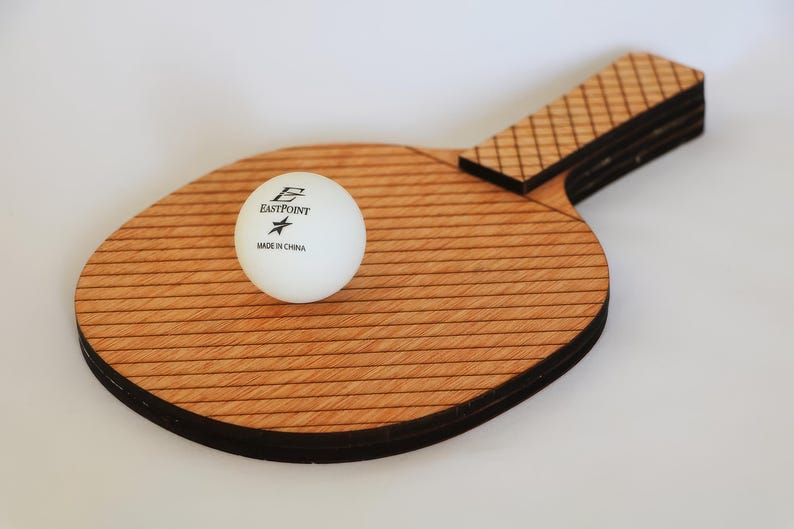 May include: A wooden ping pong paddle with a white ball. The paddle has a light brown, striped surface and a dark brown handle. The white ball has the text "EASTPOINT" and "MADE IN CHINA" printed on it.