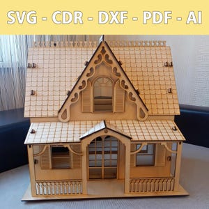 May include: A wooden dollhouse with a detailed design, featuring a gabled roof, shutters, and a porch. The text "SVG - CDR - DXF - PDF - AI" is displayed at the top. The dollhouse is made of light-colored wood.