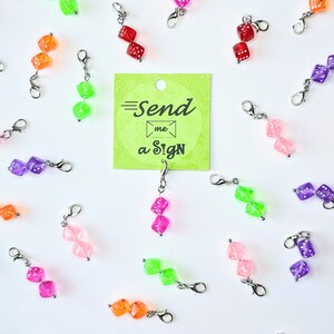 May include: A collection of colorful dice charms with silver clasps. The charms are arranged on a white background with a green card that reads "Send me a Sign".