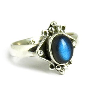 Könnte beinhalten: Ein silberner Ring mit einem blauen Labradorit-Edelstein, der in einem dekorativen, verzierten Design gefasst ist. Der Ring hat eine silberne Band und eine detaillierte Fassung mit kleinen Perlen.