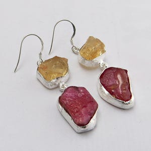 Peut inclure: Boucles d'oreilles pendantes en argent avec deux gouttes de pierres précieuses brutes. La goutte supérieure est une citrine jaune et la goutte inférieure est un rubis rose.