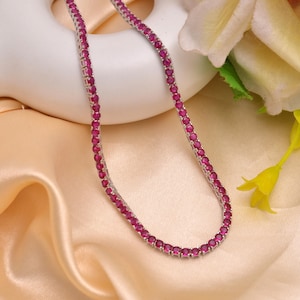 May include: A silver chain necklace with a row of small, bright red ruby stones.