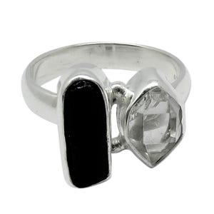 Op de afbeelding: Een zilveren ring met een zwarte en heldere edelsteen setting. De ring heeft een rechthoekige zwarte steen en een gefacetteerde heldere steen.