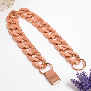 Pode incluir: Uma pulseira de corrente em ouro rosa com elos grandes e interligados. A pulseira tem um fecho e é exibida em uma superfície branca. A joia é uma peça ousada.
