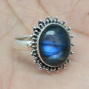 Könnte beinhalten: Ein silberner Ring mit einem blauen Labradorit-Edelstein, der in einem Perlenhalo-Design gefasst ist.