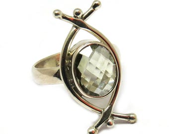 Könnte beinhalten: Ein silberner Ring mit einem klaren, facettierten Edelstein, der in einem einzigartigen, abstrakten Design gefasst ist.