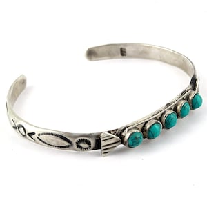 Könnte beinhalten: Ein silbernes Armband mit türkisfarbenen Steinen, die in einer Reihe angeordnet sind. Das Armband hat ein schlichtes Design mit einem sich wiederholenden Muster aus kleinen Dreiecken und Ovalen.