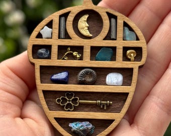 May include: A wooden acorn-shaped box with a variety of small objects inside, including a crescent moon, a star, a key, and several crystals. The box is made of light brown wood and has a natural finish.