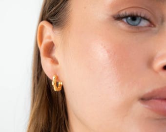 May include: A small gold hoop earring with a textured, segmented surface resembling bamboo, worn in the earlobe. The earring features a polished metallic finish and a circular design that secures through the ear with a simple clasp mechanism.