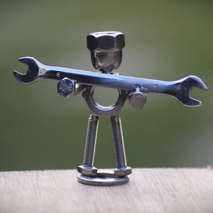 Mechaniker, der eine Schraubenschlüssel-Skulptur hält, die mit Edelstahl-Muttern und Schrauben gemacht ist